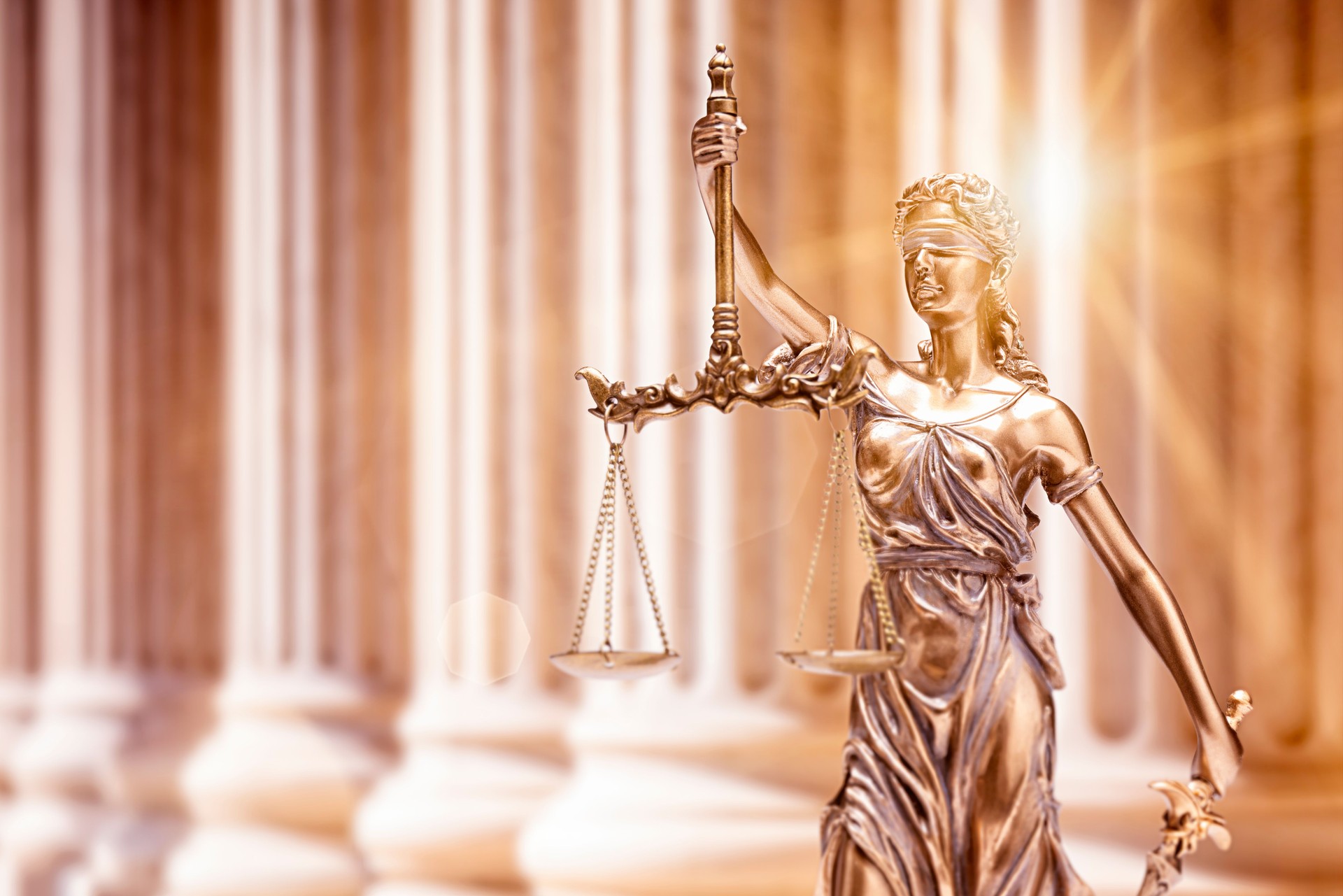 Lady Justice in front of courthouse columns with sunflare